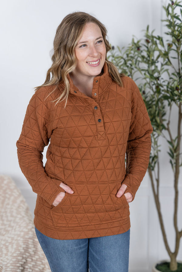 Woman wearing a brown quilted pullover with a plant in the background