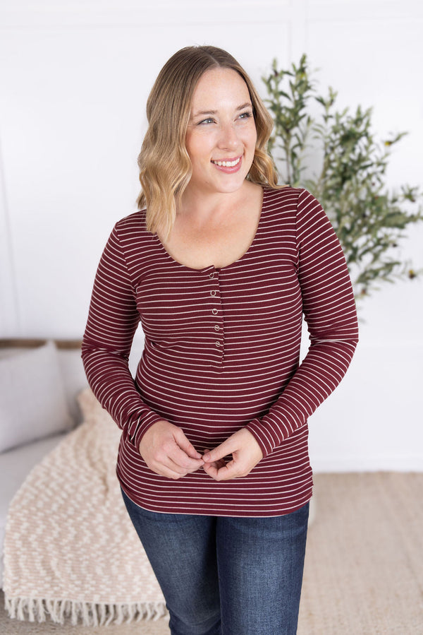 Woman wearing a maroon and white striped long-sleeve shirt in a cozy indoor setting.