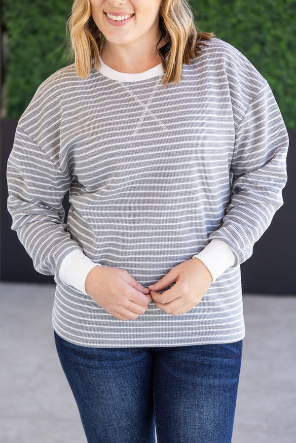 Woman wearing a gray and white striped sweater and blue jeans against a neutral background