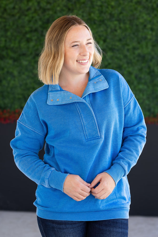 Woman wearing a blue pullover with a green wall in the background