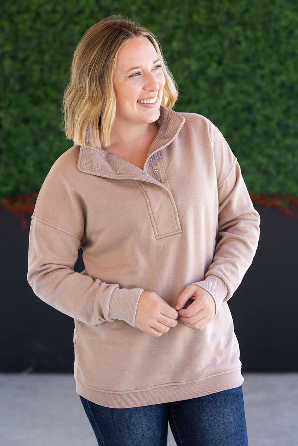 Woman wearing a beige pullover with a green wall in the background