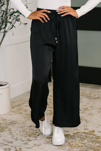 Person wearing black wide-leg pants and white sneakers indoors.