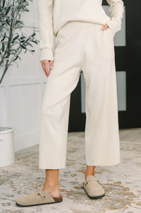 Person wearing a white outfit with wide-leg pants and beige shoes indoors.