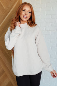 Woman wearing a light gray sweater against a white brick wall.