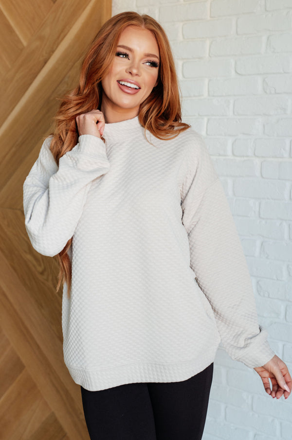 Woman wearing a light gray sweater against a white brick wall.