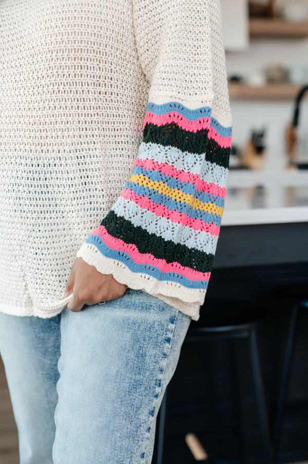 Person wearing a white sweater with colorful striped sleeves in a casual setting.