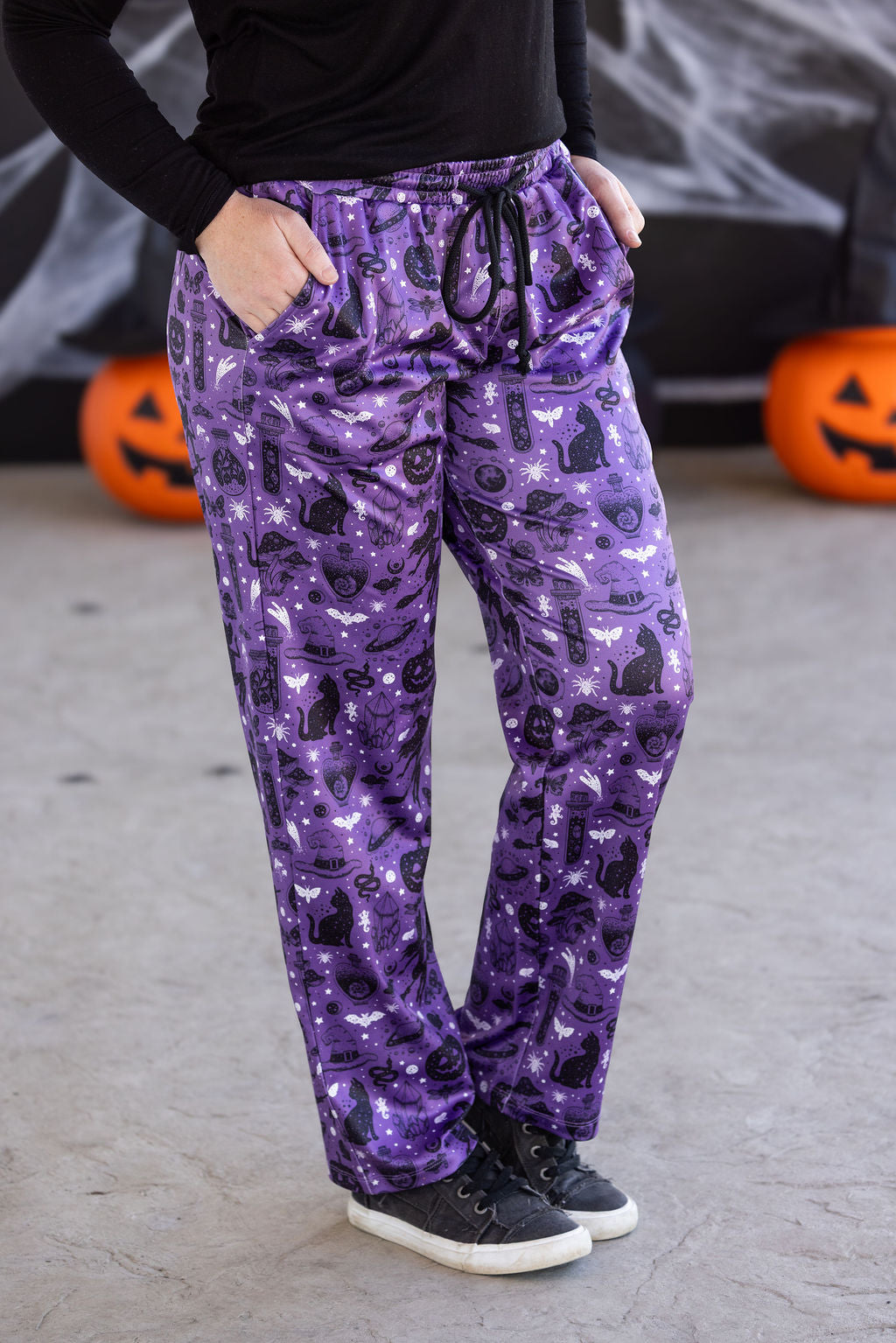 Purple Halloween-themed pants worn by a person with pumpkins and spider webs in the background.