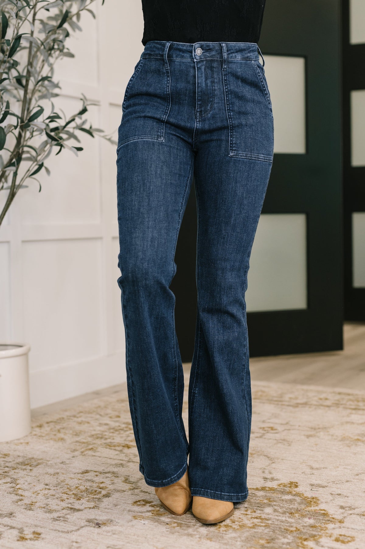 Blue jeans worn by a person standing indoors with a plant and wall in the background