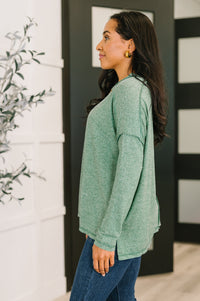 Woman wearing a green sweater and blue jeans standing indoors.