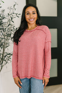 Woman wearing a pink sweater and blue jeans indoors with a plant in the background