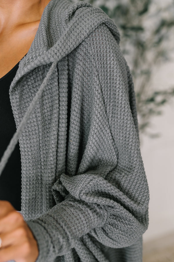 Gray knitted cardigan being worn, with a blurred background