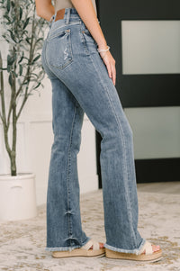 Person wearing blue jeans standing indoors with a plant in the background
