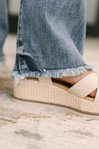 Close-up of a sandal with a woven design worn with blue jeans on a blurred background