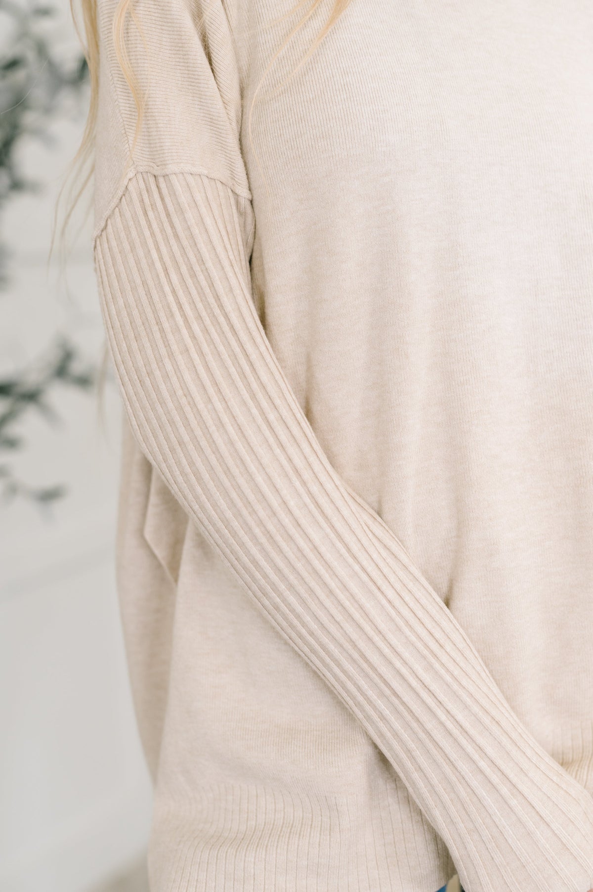 Close-up of a beige ribbed sweater sleeve against a neutral background