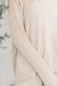 Close-up of a beige ribbed sweater sleeve against a neutral background