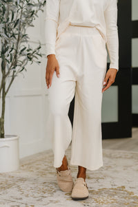 Person wearing a white outfit with wide-leg pants in an indoor setting.