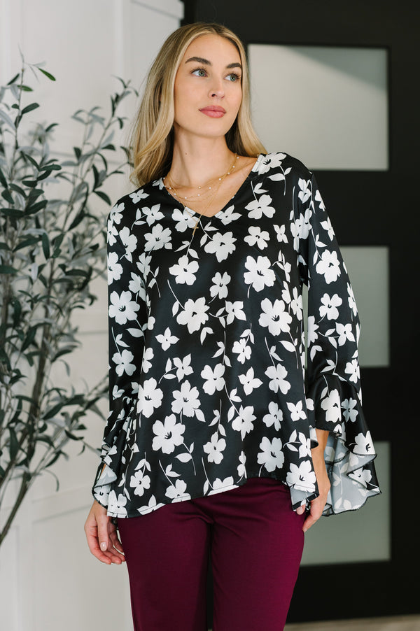 Woman wearing a black floral blouse with burgundy pants indoors.
