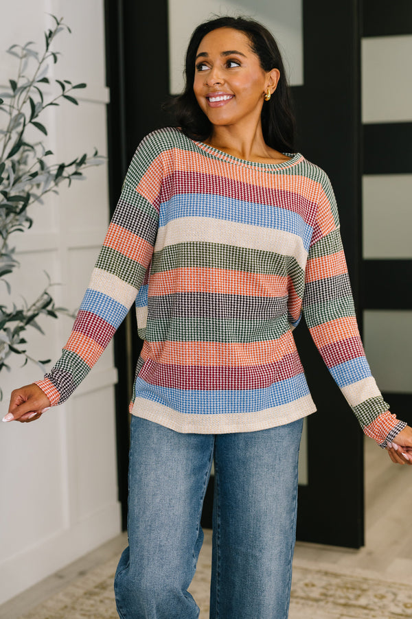 Woman wearing a colorful striped sweater and jeans indoors.
