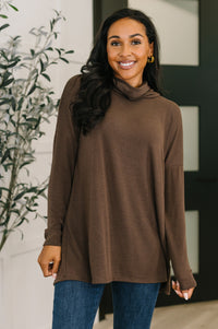 Woman wearing a brown turtleneck sweater and blue jeans indoors.