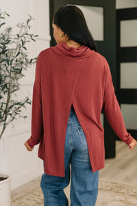 Person wearing a red sweater and blue jeans standing indoors with a plant in the background