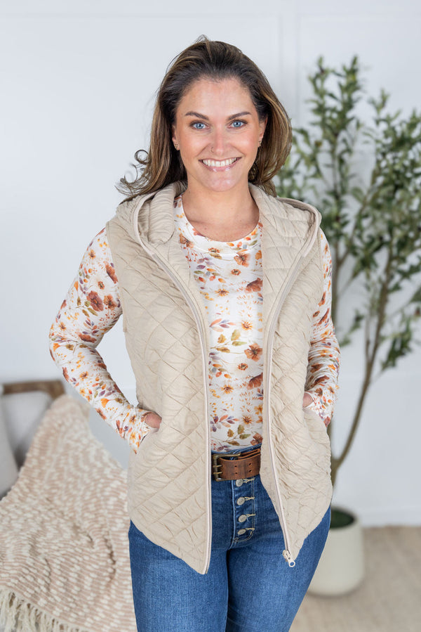 Woman wearing a beige quilted vest over a floral shirt with a neutral background