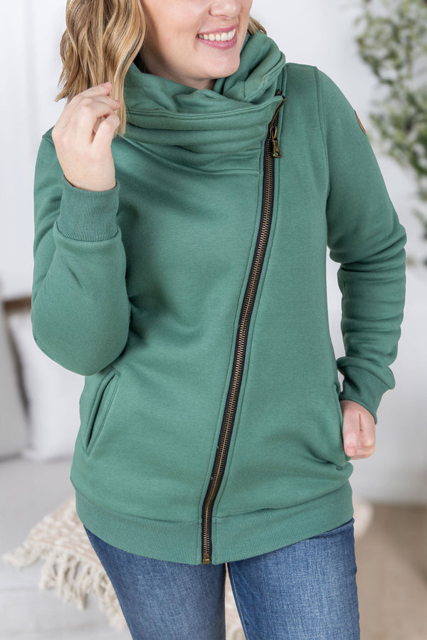 Woman wearing a green zip-up hoodie with a blurred indoor background