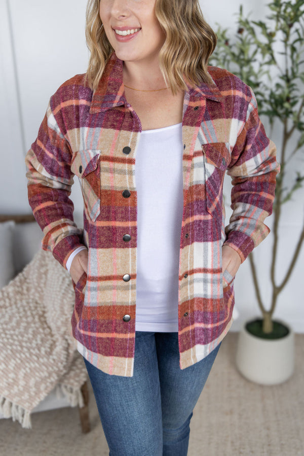 Woman wearing a plaid shirt over a white top with blue jeans indoors.