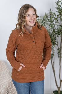 Woman wearing a brown quilted pullover with a plant in the background
