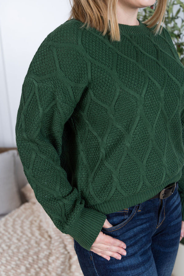 Person wearing a green cable knit sweater with a blurred background