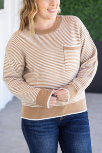 Woman wearing a beige and white striped sweater with a pocket, standing outdoors.