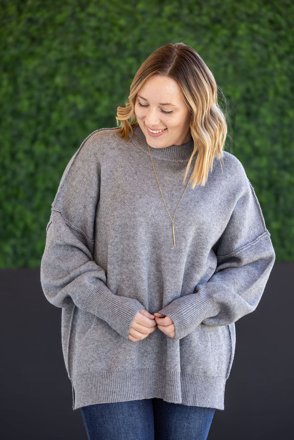 Woman wearing a gray sweater against a green wall.