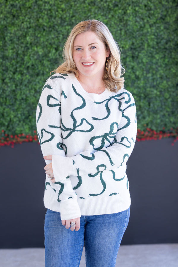 woman wearing a white sweater with green ribbon pattern 