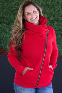 Woman wearing a red cowl-neck sweater with a zipper against a green hedge background