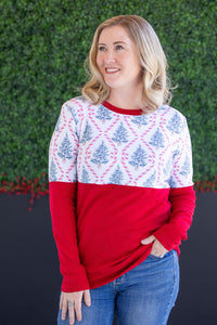 Woman wearing a red and white patterned sweater with blue jeans against a green hedge background