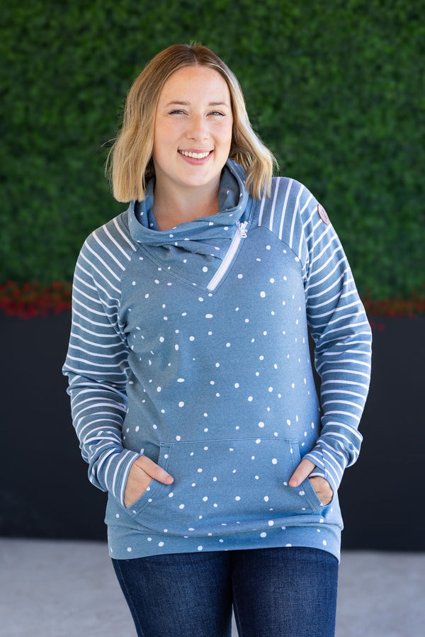 Woman wearing a blue polka dot hoodie with striped sleeves against a green wall.