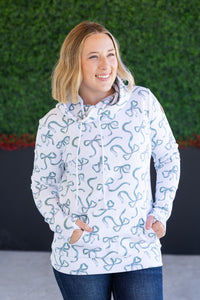 Woman wearing a white hoodie with blue patterns against a green hedge background