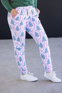 Person wearing white jogger pants with blue and pink tree pattern on a gray floor.