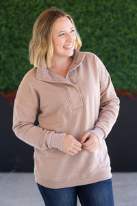 Woman wearing a beige pullover with a green wall in the background
