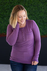 Woman wearing a purple long-sleeve shirt against a green and black background