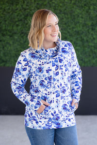 Woman wearing a blue floral pullover against a green hedge background