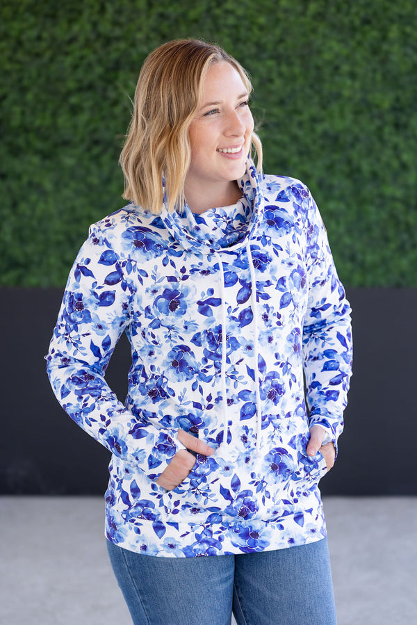 Woman wearing a blue floral pullover against a green hedge background