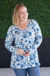 Woman wearing a blue floral long-sleeve top against a green wall.