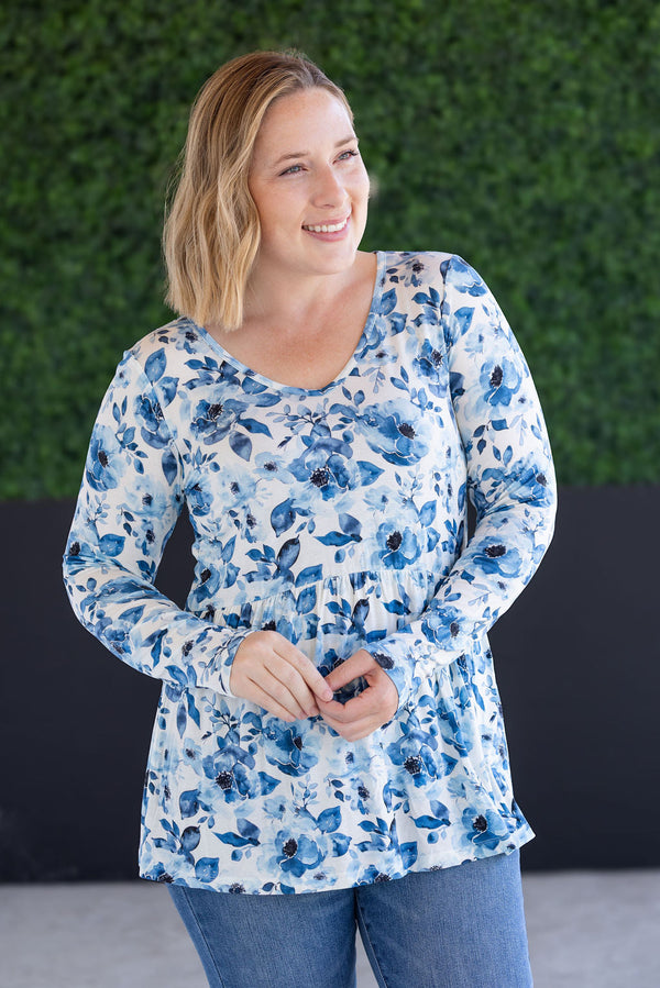 Woman wearing a blue floral long-sleeve top against a green wall.