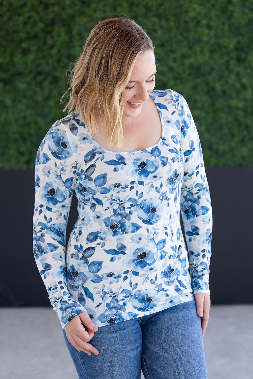 Woman wearing a blue floral long-sleeve top against a green wall.