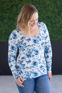 Woman wearing a blue floral long-sleeve top against a green wall.
