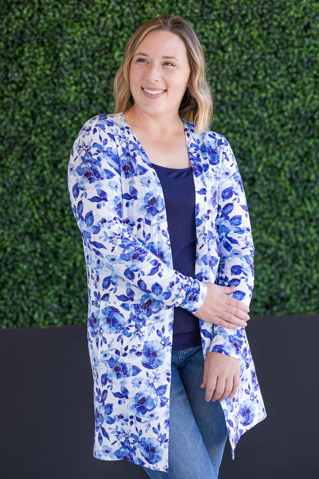 Woman wearing a blue floral cardigan against a green hedge background