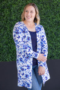 Woman wearing a blue floral cardigan against a green hedge background
