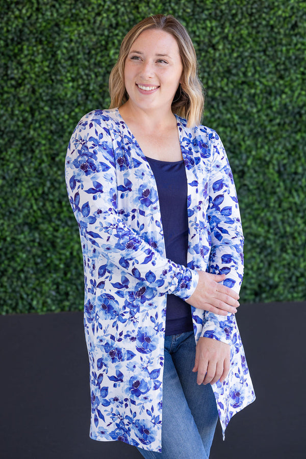 Woman wearing a blue floral cardigan against a green hedge background