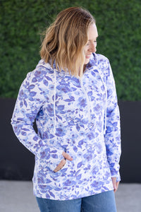 Woman wearing a blue floral patterned jacket against a green wall.