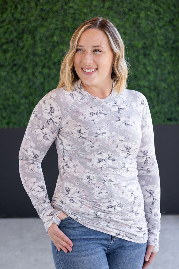 Woman wearing a floral long-sleeve top and jeans against a green wall.